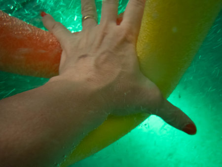 Aqua aerobics image of woman's hand reaching through swimming pool water energetically to grasp pool noodle.の写真素材