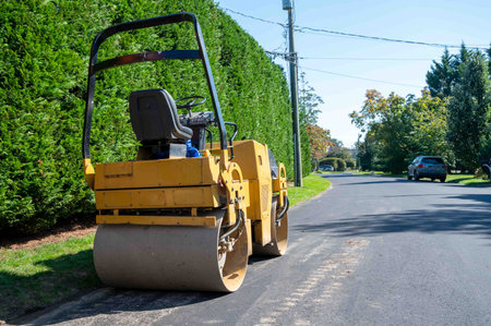 No people in the image of a roller on the side of a quiet suburban street. Asphalt paving equipment...