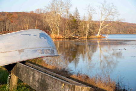 A vintage metal canoe rests on a wooden rack by an idyllic autumn woodland lake in golden hour sunlight with trees reflected in the water. Fall colors, no people, copy spaceの写真素材