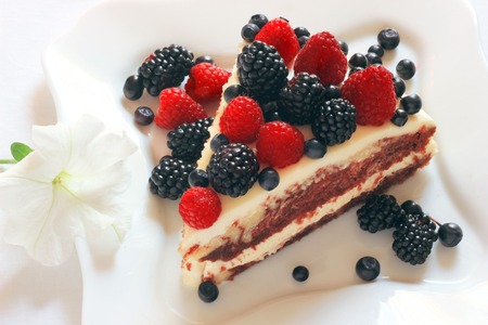 Creamy sweet cake with chocolate and cream, garnished with blueberries and raspberries on a white tableclothの写真素材