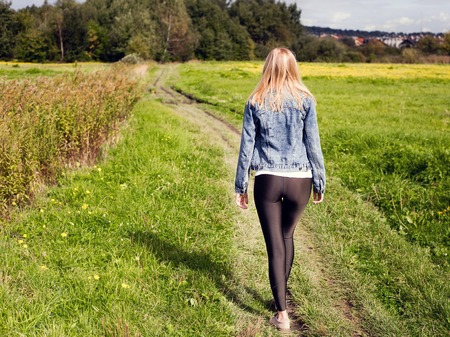 girl dressed in leggings and denim jacket walking on country roadの写真素材