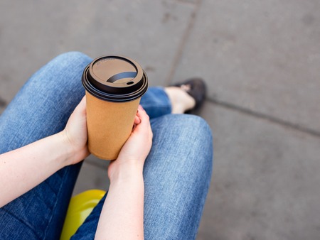 Trendy cool hipster woman or young girl holds take away to go cup of coffee on the street, concept life on the go, warm and cosy drinkの写真素材