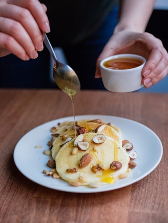 Woman pouring honey on tasty pancakes with nuts on a wooden table. Still life in a rustic style....