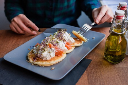 Woman having a pancake with salmon and sourcream in a restaurant. Tasty homemade breakfast.の写真素材