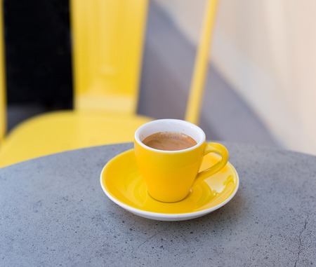 Espresso coffee in yellow cup on the stone table with blurred background