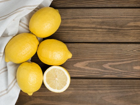 Whole and sliced lemons with white fabric on brown wooden background. Organic fresh citrus fruits,...