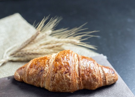 Fresh french croissant with ears of wheat on black background on the table.の写真素材