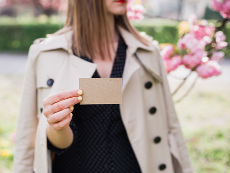 Woman showing business card. Hand holding a craft visit card, gift, ticket, pass, present close up on nature backgroundの写真素材