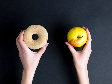 hands hold donut and apple on dark backgroundの写真素材