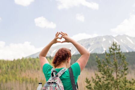 Girl making a heart-shape with mountain landscape in the background. Copyspace. A young pretty...