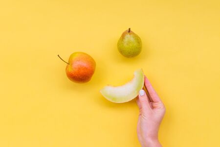 Smiling fruits on a yellow background. Woman's hand hold a Slice of melon. Melon, apple, pearの写真素材