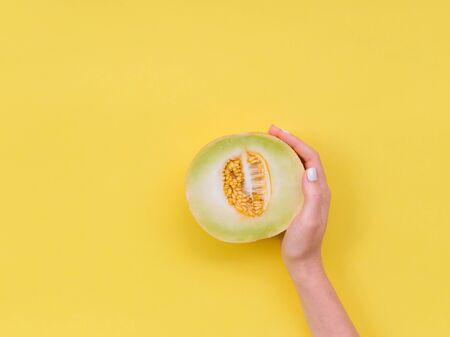 Womans hand hold a cut melon in half. Ripe melon cut in half on a bright yellow background.の写真素材