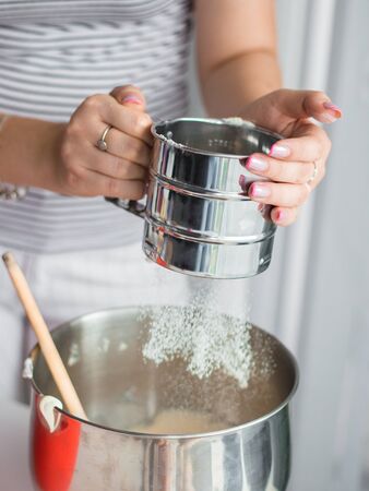 Hand holds metal flour sifter, a sieve sprinkled flour. Sifting flour. Preparation for baking.