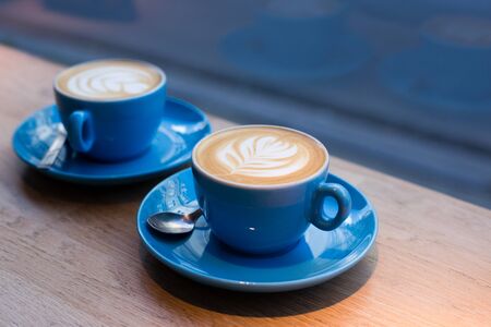 Two cups of cappuccino with latte art on wooden table, blue ceramic cup in cafe. Cafe culture.の写真素材