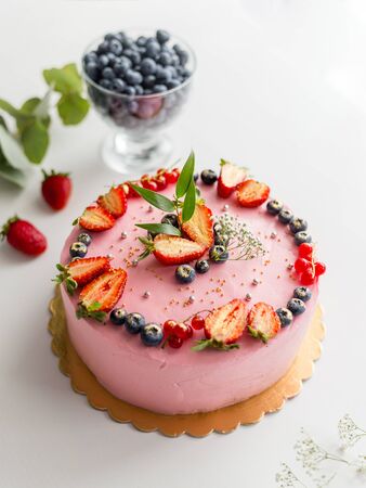 Homemade pink birthday cake decorated with berries: strawberries, blueberries, red currant and flowers. Food concept. Girl birthday or wedding cream cheese pink cake on white backgroundの写真素材
