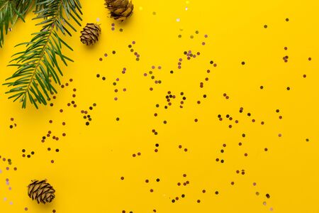 Frame made of cones and pine branches. Yellow Christmas background with multicolored confetti. Flat lay style.の写真素材