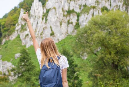 Young woman with backpack giving thumbs up. Trekking and tourism concept. Copyspace. A young pretty girl standing on a background of mountainsの写真素材