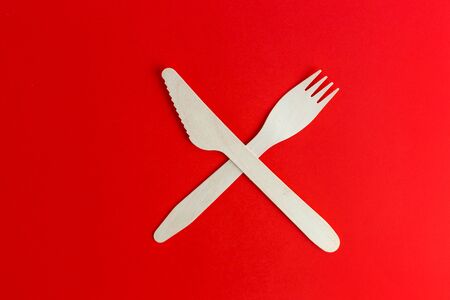 Wooden disposable fork and knife on red background, recycling and eco friendly concept. Zero waste,...