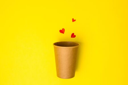 Open Craft paper cup with paper hearts on a yellow background. Flat lay. Creative Minimal food concept. Copy space, drink cup package mockupの写真素材