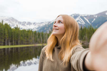 The girl tourist taking selfie in the mountain lake. Looking up and smile. Travel and active life concept. Outdoorsの写真素材
