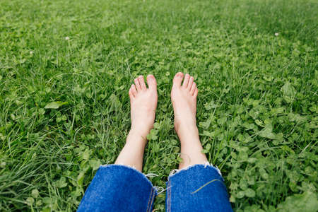 Legs woman relaxing on grass. Female feet on green grass background. Beautiful barefoot legs in the morning dew on the grass.の写真素材