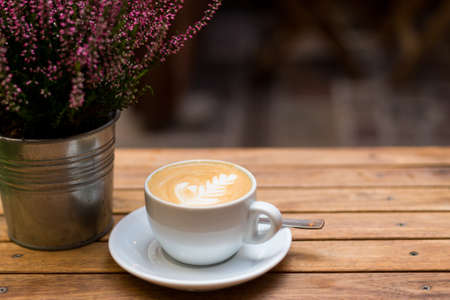 One cup of cappuccino with latte art on wooden table, white ceramic cup, place for text. Terrace...