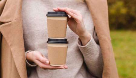 Woman holds two paper coffee cups. Take away or delivery concept. Copy space. Autumn lifestyle....