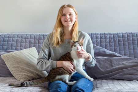 Woman holding homeless cat and sitting on the sofa at home in the living room. Concept of...