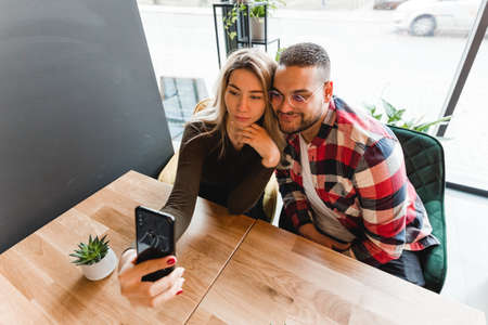 Beautiful Friends Taking Photos In Cafe. Happy young couple is doing selfie, smiling and sitting at...