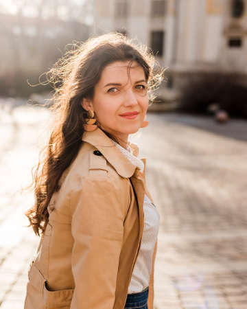 Beautiful young woman at city street. Happy tourist girl walking outdoors. Spring portrait of pretty...