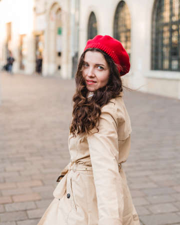 Beautiful young woman at city street. Happy tourist girl walking outdoors. Spring portrait of pretty brunette female posing in old town. Follow meの写真素材