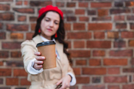 Close-up portrait of attractive pretty stylish cheerful curly-haired brunette girl holding at paper-cup coffee isolated on red brick background, Happy woman outdoors.の写真素材