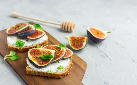 Two Sandwiches with cream cheese, figs and leaves salad served on the wooden board on gray...