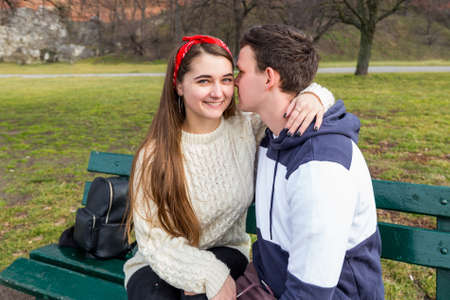 Young couple sitting on a wooden bench. Beautiful sunny day. Young happy people relaxing outdoor in...