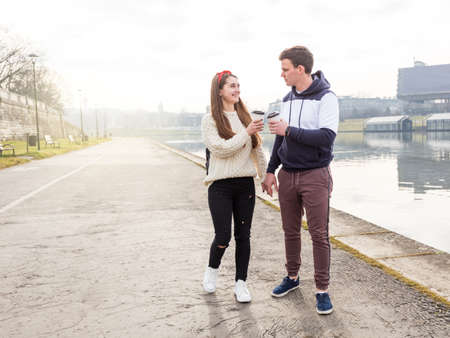 Young couple in love outdoor. Travelers with cups of coffee are walking in spring park.