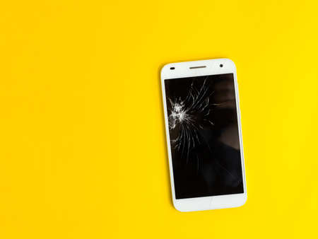 Modern touch screen smartphone with broken screen on yellow background. Flat lay style. Top view. Place for text.の写真素材