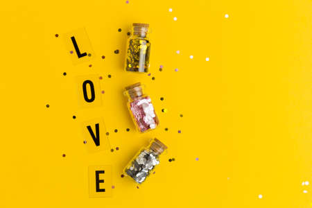 Love in black letters on a yellow background with confetti. Flat lay style. Concept specially offer. Three small glass bottles with confettiの写真素材