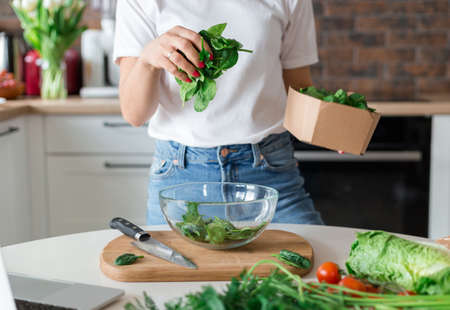 Close up woman in white t-shirt cooking salad with motion effect at home kitchen. Process of cooking healthy food, vegetable salad concept. Menu, recipe book bannerの写真素材