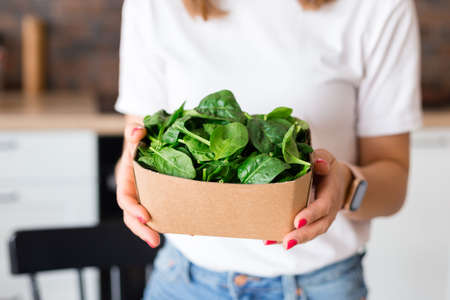 Woman in white t-shirt holding a green spinach in recycling ecology packing. Raw food diet and healthy eating concept. Baby foodの写真素材