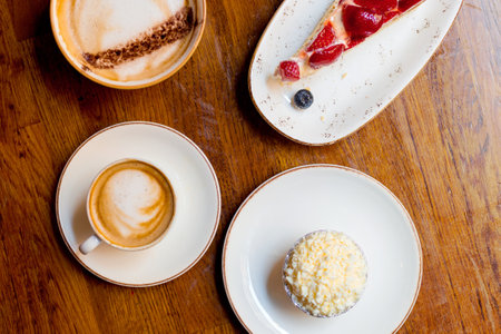 Piece of homemade strawberry cake with muffin and two cups of cappuccino with latte art on wooden background. Small and big ceramic cups. Top viewの写真素材