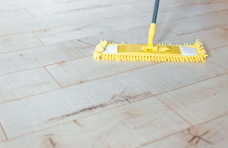 Microfiber yellow mop isolated on white wooden floor background, closeup, indoors