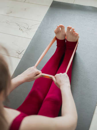 Resistance band exercise at home. Woman doing pilates workout using elastic strap pulling with arms...