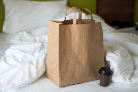 Delivery food craft bag with cup on the bed on sunny day. Delivery in any weather around the clock to the client. Fast food eco packaging with big breakfast setの写真素材