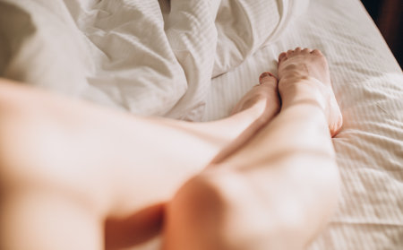 Woman legs on the bed in white bedclothes, Sunny rays. Cropped image of erotically lying on bed beautiful woman in bedroom.の写真素材