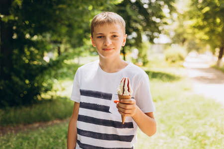 Teenager boy eating ice-cream cone on green nature background. Summer, junk food and people conceptの写真素材