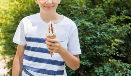 Teenager boy eating ice-cream cone on green nature background. Summer, junk food and people conceptの写真素材