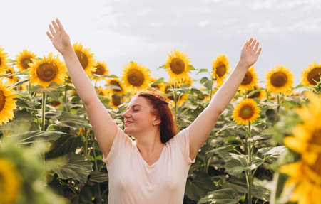 Happy free woman opened arms walking in blooming sunflower field. The concept of freedom. Young woman hand up on nature backgroundの写真素材