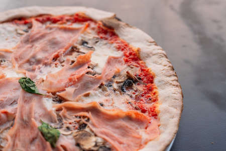 Baked pizza with prosciutto and mushrooms with red sauce and melted cheese on a black wooden...