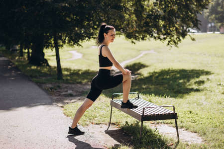 Portrait of fit sporty young woman doing stretching in city park. Outdoor workout. Sport and healthy active lifestyle concept. Black clothing for sportsの写真素材