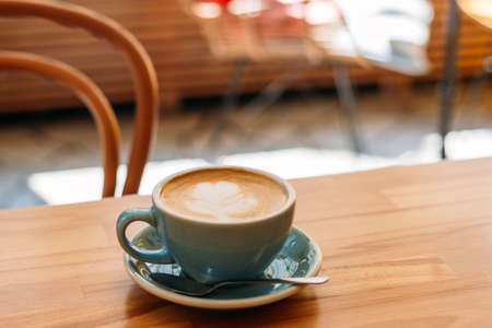 One Cup of cappuccino with latte art. Coffee in blue cup on wooden table in cafe. Concept of easy breakfast.の写真素材